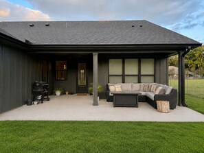 A modern house with a covered porch, a sectional sofa, and a grill outside.