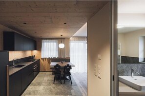 A modern kitchen with a dining area, wooden ceiling, and a view into a bathroom. - Cozy chalet with a hot tub and sauna in the Dolomites (Naz BZ)