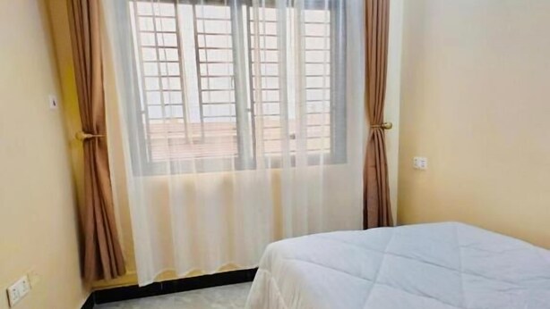 Ein Schlafzimmer mit einem Bett, einem Fenster mit Vorhängen und einem Fliesenboden.