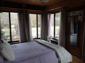 Ein Schlafzimmer mit einem großen Bett, einer Holzbalkendecke und Blick ins Freie durch ein Fenster.
