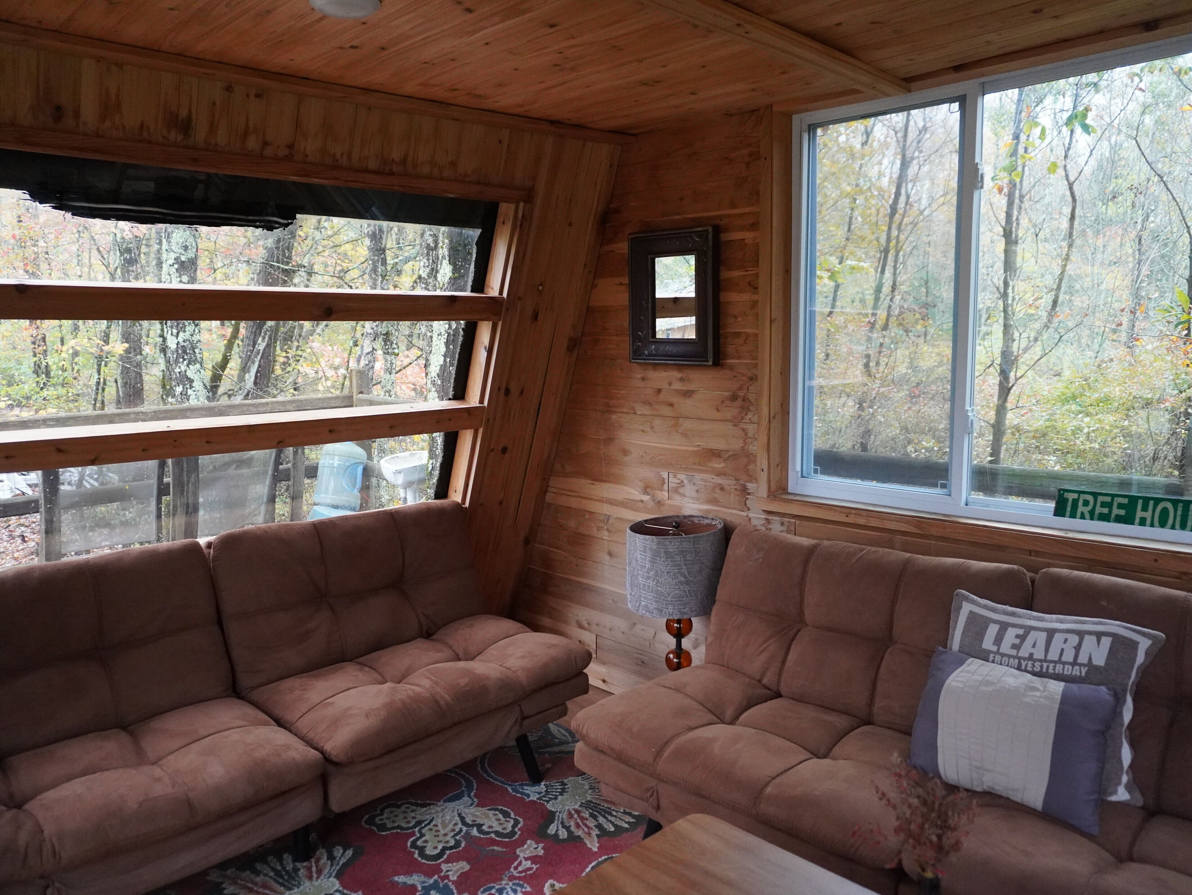 A cabin interior with two couches facing a window, a small rug, and a wall-mounted lamp.