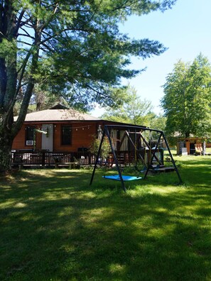 A wooden cabin with a swing set in a grassy yard. - Lovely 3-bedroom cottage with a 3-level treehouse (Woodbourne)