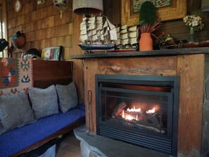 A cozy interior with a fireplace, wooden walls, a blue sofa, and decorative items like a ship model and a vase. - Lovely 3-bedroom cottage with a 3-level treehouse (Woodbourne)