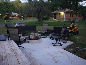 An outdoor patio with a fire pit, seating, and a lawnmower. - Lovely 3-bedroom cottage with a 3-level treehouse (Woodbourne)