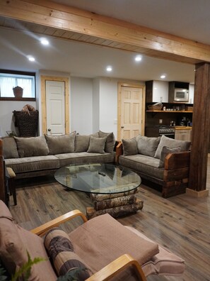 A living room with a sectional sofa, a glass coffee table, and a kitchen area with a microwave. - Lovely 3-bedroom cottage with a 3-level treehouse (Woodbourne)