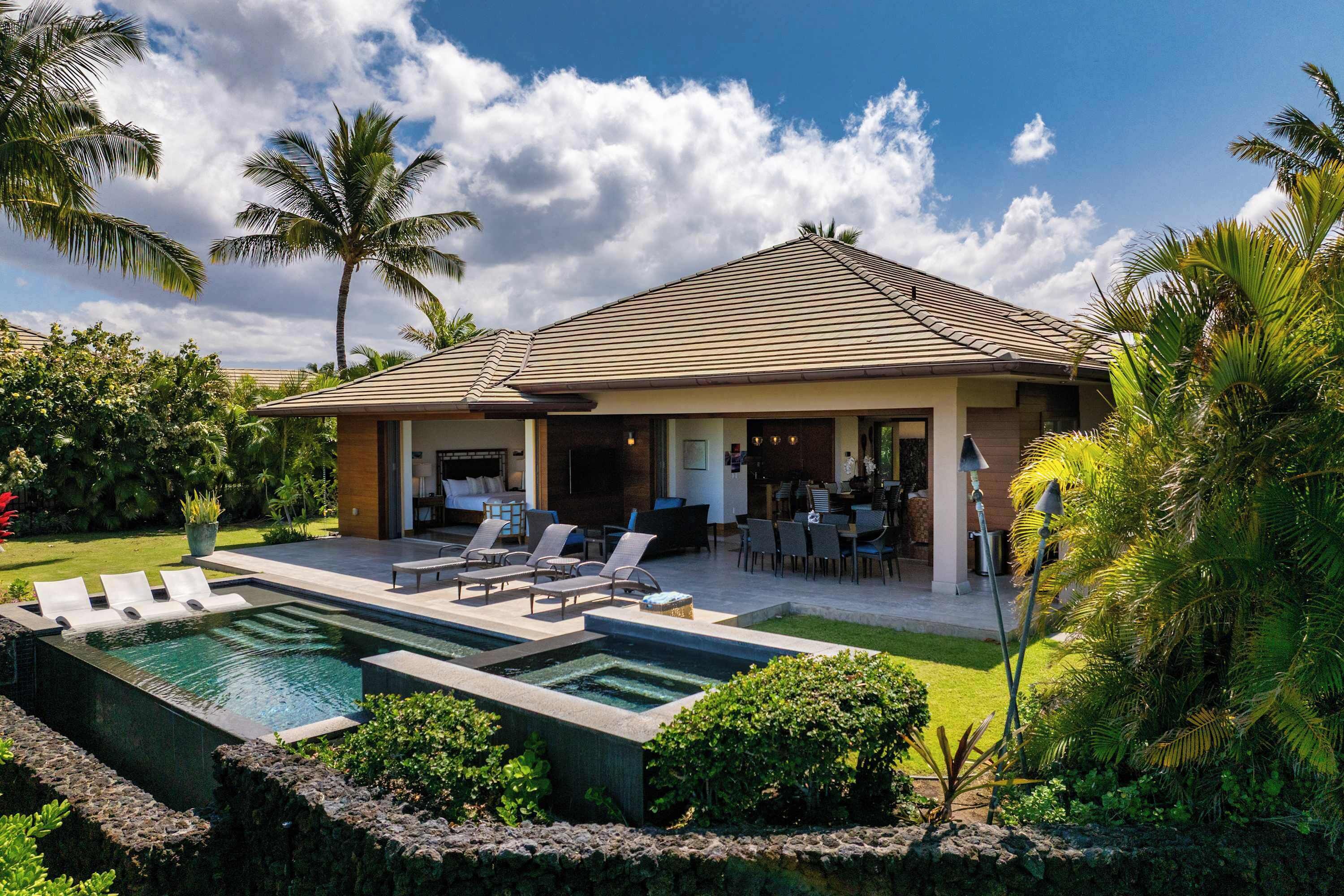 A two-story house with a swimming pool, outdoor seating, and tropical landscaping.