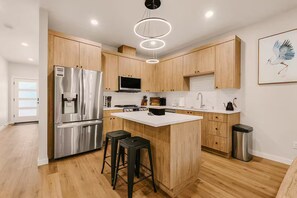 Een moderne keuken met houten kastjes, roestvrijstalen apparatuur, een centraal eiland met krukken en een hangende lamp.