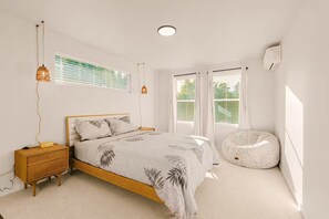 Ein Schlafzimmer mit Bett, Nachttisch, Lampe, Fenster und einer Wand-Klimaanlage.