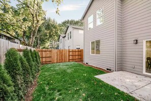 A residential backyard with a wooden fence, a lawn, and a house with a garage. - Scandinavian 4BR - King Suite · EV Plug · Sleeps 10 (Gresham)