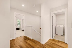 Un pasillo con suelo de madera, paredes blancas y un área de lavandería con lavadora.