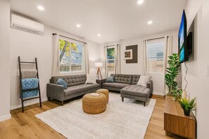 Een moderne woonkamer met een grijze modulaire bank, een klein bijzettafeltje en een aan de muur bevestigde televisie.