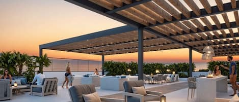 An outdoor patio area with wooden pergolas, seating arrangements, and a view of the ocean at sunset.