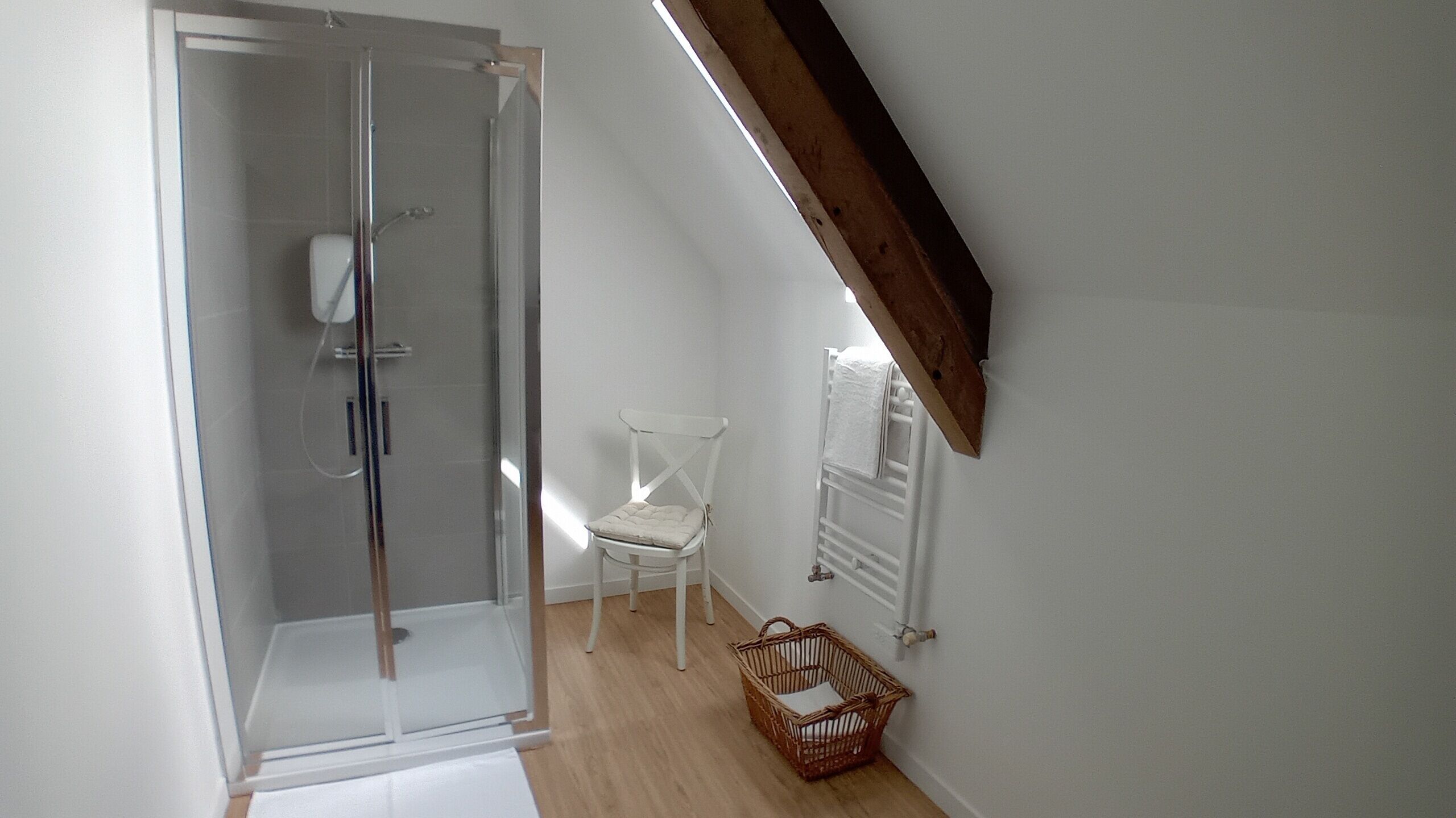 Una habitación con cabina de ducha de vidrio, una silla blanca y una cesta de mimbre.