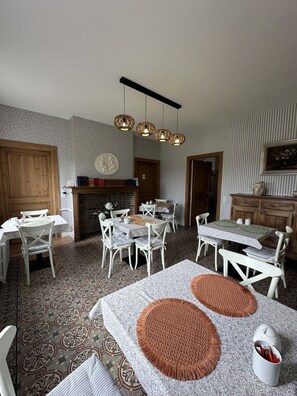 A dining area with a fireplace, a kitchen in the background, and a dining table with chairs.