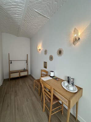 Una habitación con una mesa de comedor de madera, sillas, una cafetera y luces fijadas a la pared.
