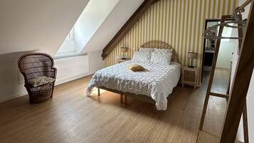 A bedroom with a sloped ceiling, a bed with a white duvet, a wicker chair, and a hanging light fixture.