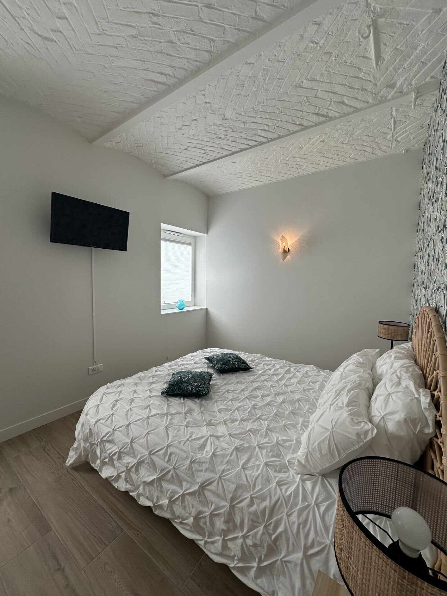 Une chambre à coucher comprenant un lit, un téléviseur fixé au mur, une fenêtre et un luminaire fixé au mur.