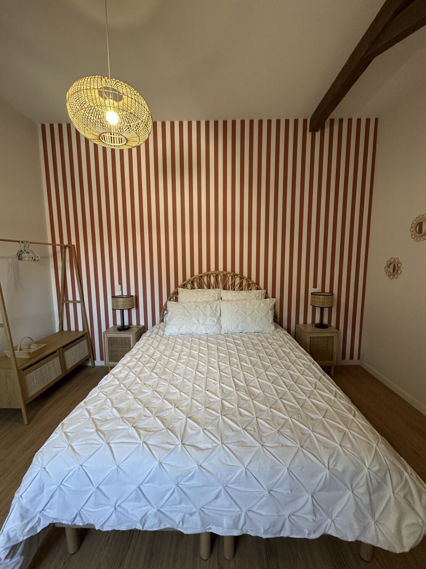 Un dormitorio con una cama grande, papel tapiz a rayas, un lámpara colgante y suelo de madera.