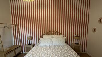 Un dormitorio con una cama grande, papel tapiz a rayas, un lámpara colgante y suelo de madera.