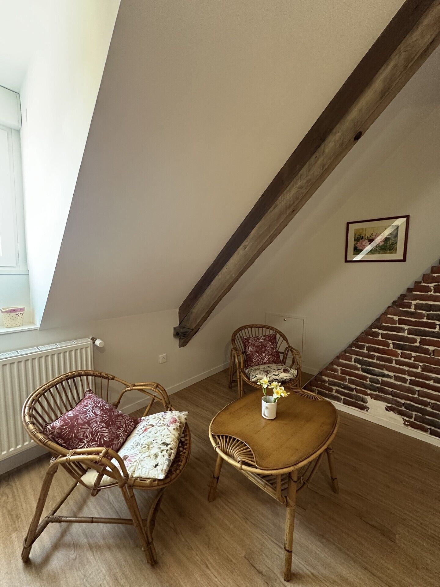 A room with a sloped ceiling, a brick wall, a wooden table with chairs, and a radiator.