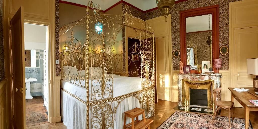 Un lit à baldaquin orné de motifs métalliques complexes, une cheminée et un miroir au mur.
