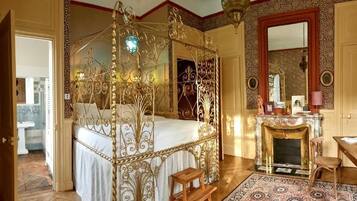 Un lit à baldaquin orné de motifs métalliques complexes, une cheminée et un miroir au mur.