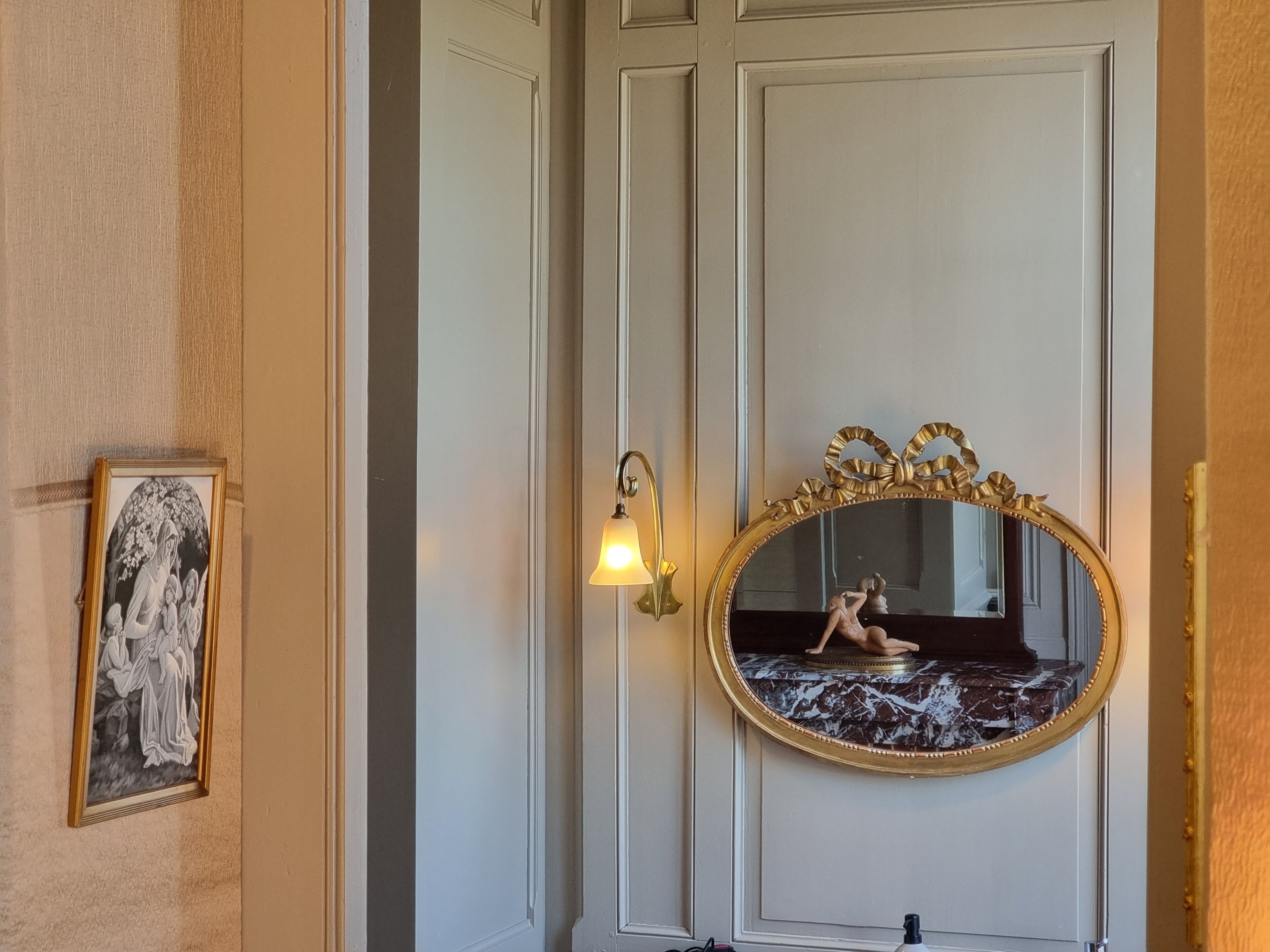 Et værelse med en dør, et spejl på væggen, et billede i ramme og en lampe monteret på væggen.