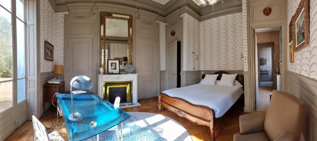 Ein Zimmer mit einem Bett, einem Schreibtisch, einem Stuhl, einem Kamin und einem großen Fenster.