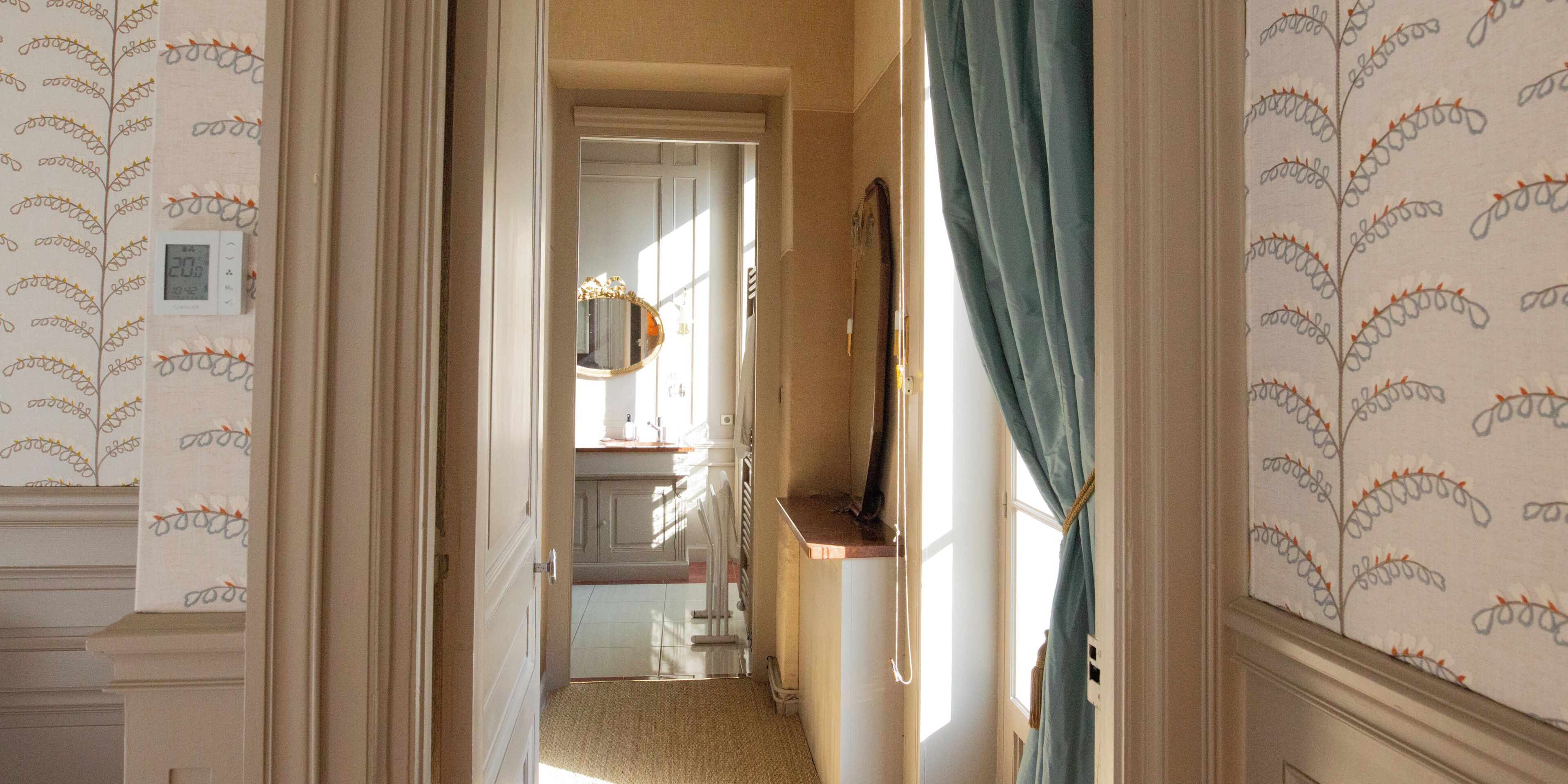 A hallway with patterned wallpaper, a mirror, and a door leading to a bathroom.