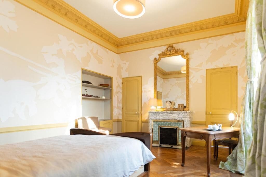 Een hotelkamer met een bed, een bureau, een open haard en een grote spiegel.
