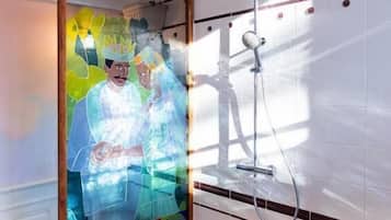 Een douche met een glazen deur, een houten vloer en een plafondlamp.