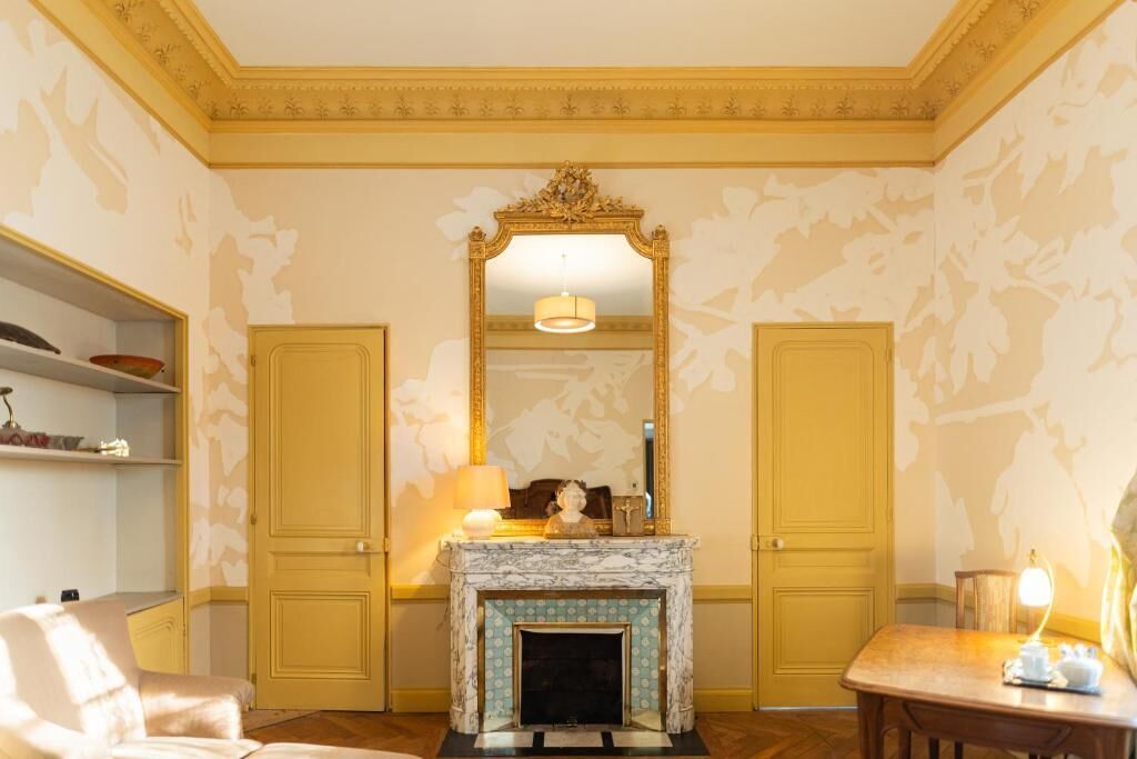 Ein Zimmer mit Kamin, Spiegel und einem Tisch mit Lampe.