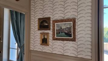 Een kamer met behang met patroon, een raam met blauwe gordijnen en drie ingelijste foto’s aan de muur.