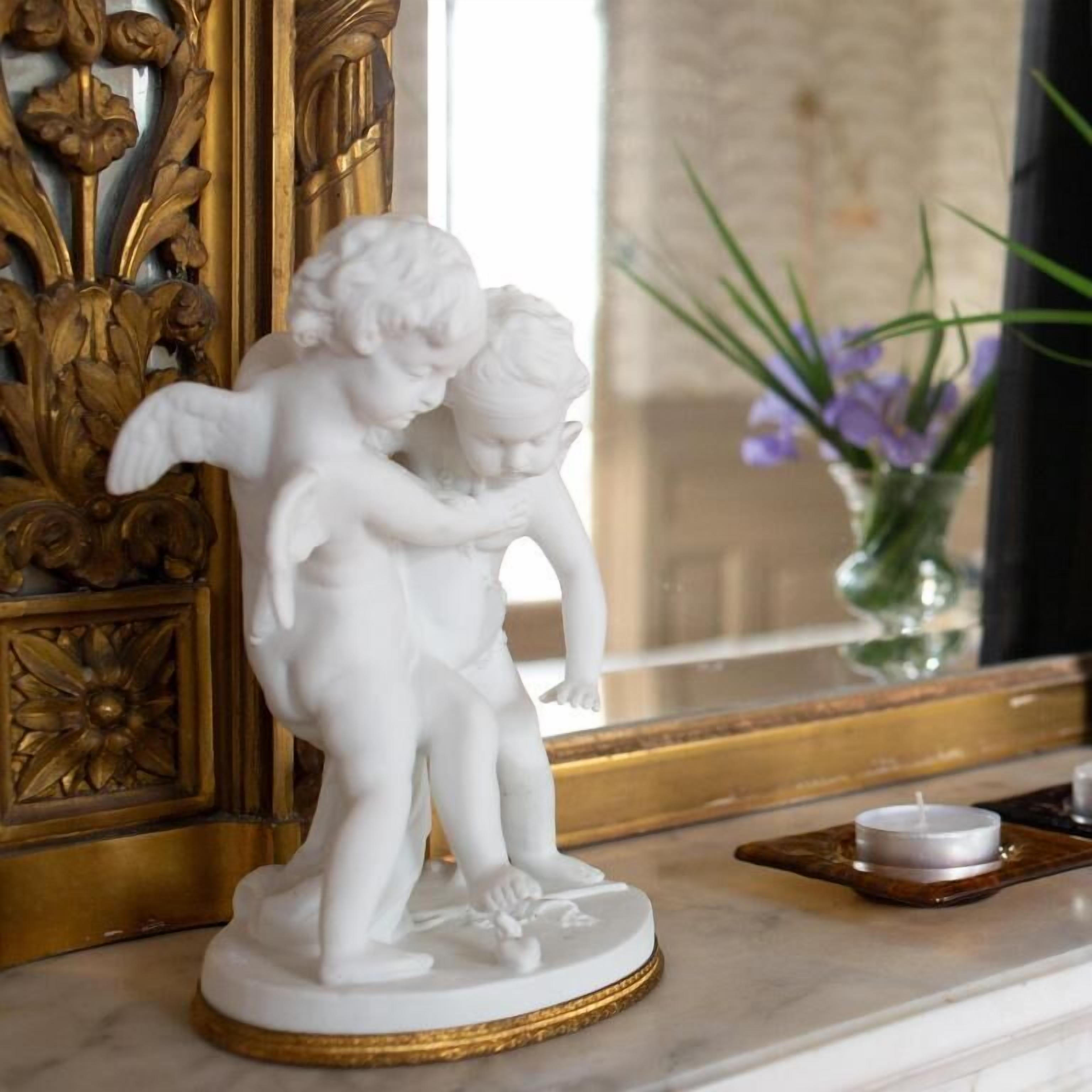Eine weiße Marmorstatue von zwei Cherubinen auf einem Sockel, platziert auf einer Marmorfläche mit einem goldrahmigen Spiegel und einem Blumenvasen mit violetten Blumen im Hintergrund.