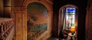Una habitación con un mural, una escalera, un ventanal con vistas y una lámpara.