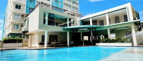 A hotel with a swimming pool, a covered area, and a multi-story building with balconies.