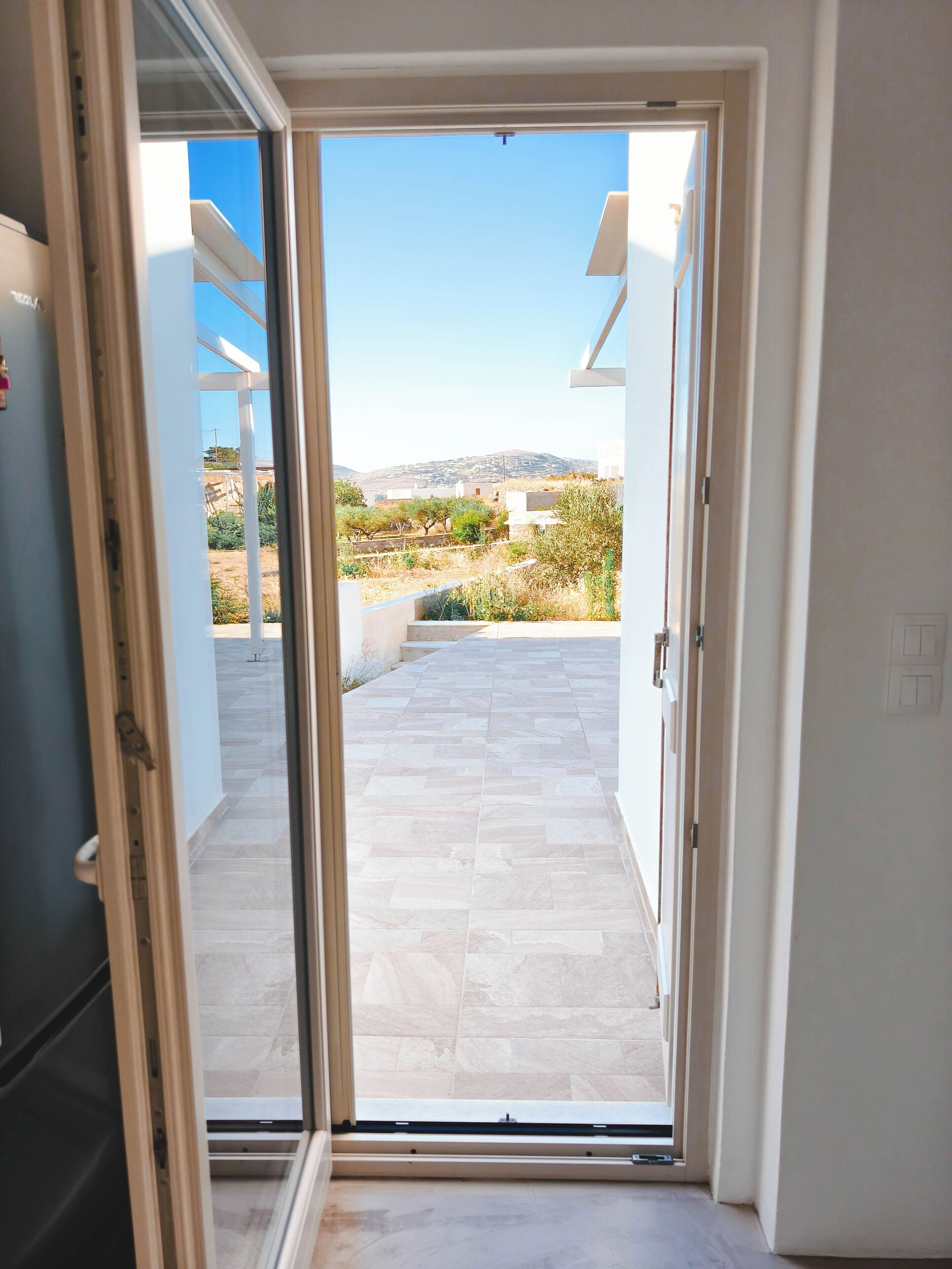 On aperçoit, à travers une porte-fenêtre coulissante, un patio extérieur doté d’un sol carrelé et surplombé d’un ciel dégagé.