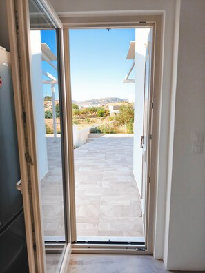 Vista a través de una puerta corrediza de vidrio a un patio exterior con suelo de baldosas y cielo despejado.