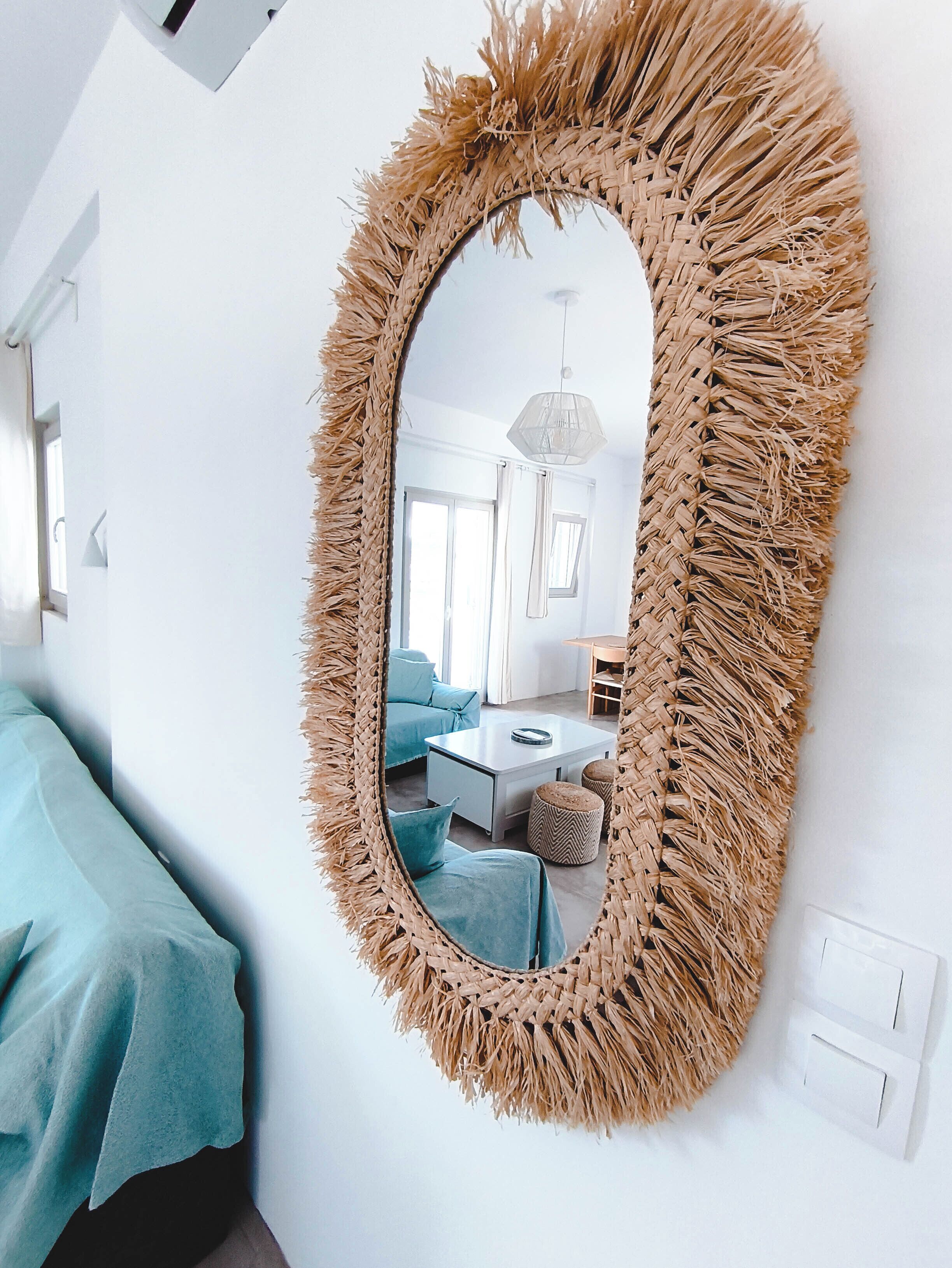 Une pièce avec un grand miroir tissé accroché au mur, un canapé bleu et une table basse blanche.