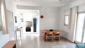 Ein geräumiger Wohnbereich mit Esstisch, Sitzgelegenheiten, einer Pendelleuchte und einer Küche im Hintergrund.