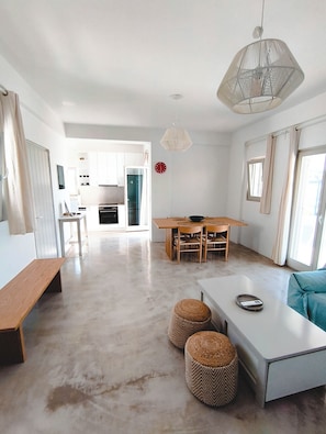 A spacious living area with a dining table, seating, a hanging light fixture, and a kitchen in the background.