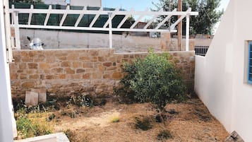 A courtyard with a white pergola, stone walls, and a small bush.