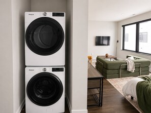 Ein Waschbereich mit zwei Whirlpool Waschmaschinen, einer Couch, einem Fernseher und einem Fenster.