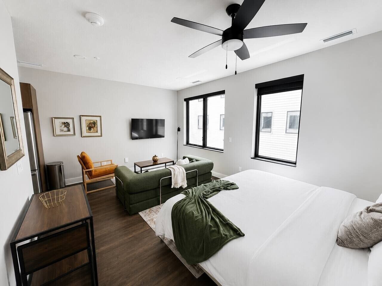 A modern hotel room with a bed, a sofa, a desk, and a ceiling fan.