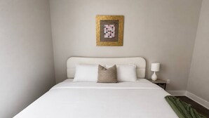 Een hotelkamer met een bed, kussens, een nachtkastje, een lamp en een lijst aan de muur.