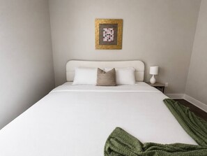 A hotel room with a bed, pillows, a nightstand, a lamp, and a framed picture on the wall. - Sleepover | Urban Studio + Gym/Sauna - Omaha (Omaha)