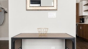 Een eetruimte met een tafel en stoelen, een spiegel aan de muur, en een keuken op de achtergrond.