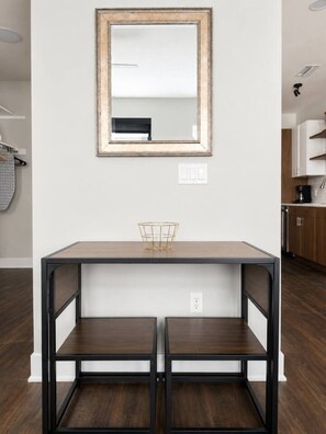 A dining area with a table and chairs, a mirror on the wall, and a kitchen in the background. - Sleepover | Urban Studio + Gym/Sauna - Omaha (Omaha)