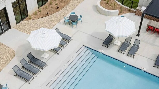 Een zwembad met ligbedden en parasols, een tafeltje met stoelen, en een zwembad met baanmarkeringen.