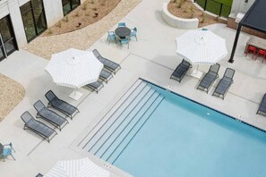 A pool area with lounge chairs and umbrellas, a small table with chairs, and a pool with lane dividers. - Sleepover | Urban Studio + Gym/Sauna - Omaha (Omaha)